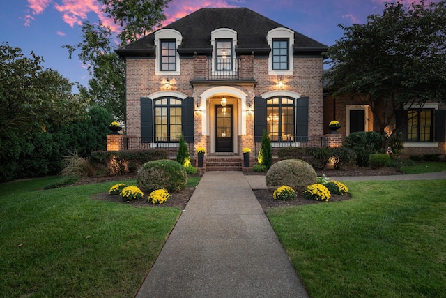 french country inspired facade featuring roof with shingles, a front lawn, french doors, and brick siding