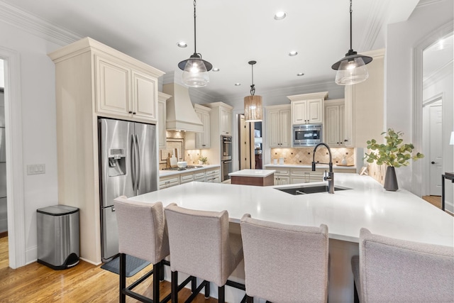 kitchen with custom range hood, appliances with stainless steel finishes, cream cabinetry, light wood-type flooring, and a sink