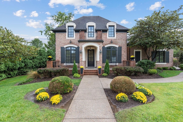 french provincial home with a front yard, brick siding, and roof with shingles