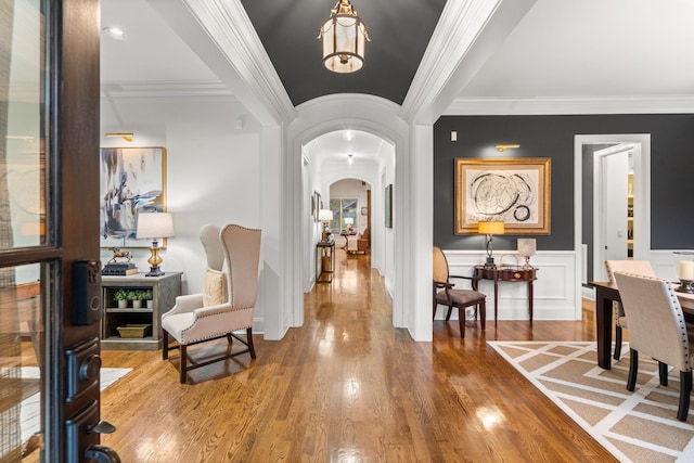 entryway featuring arched walkways, a wainscoted wall, ornamental molding, wood finished floors, and a decorative wall