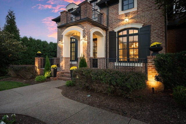 exterior entry at dusk with a balcony, a porch, and brick siding