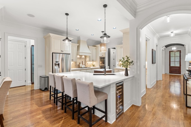 kitchen with arched walkways, premium range hood, light countertops, appliances with stainless steel finishes, and light wood-type flooring