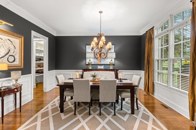 dining room featuring ornamental molding, wood finished floors, visible vents, and a notable chandelier