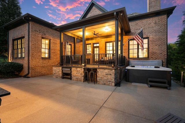 back of house at dusk with outdoor dry bar, brick siding, a chimney, and a patio area