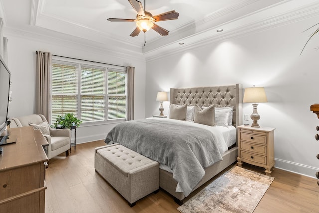 bedroom with crown molding, baseboards, a raised ceiling, and light wood-style floors