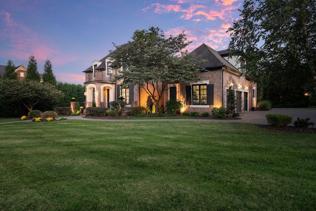 french country inspired facade featuring driveway, a garage, a front lawn, and brick siding