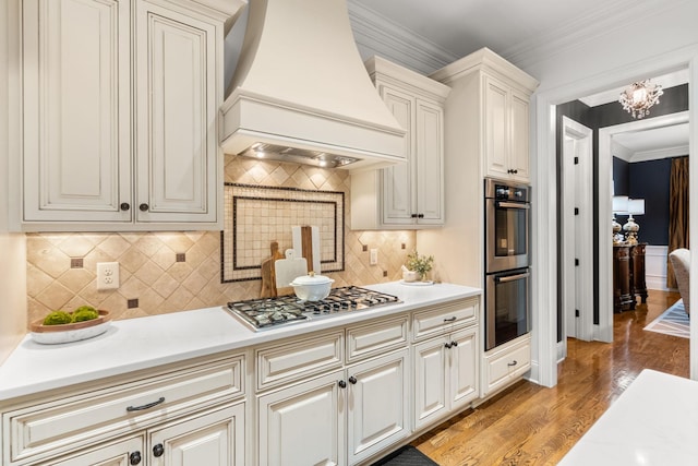 kitchen featuring stainless steel appliances, premium range hood, light countertops, light wood finished floors, and crown molding