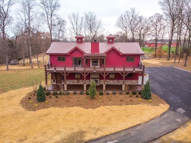 view of front of house featuring stone siding, metal roof, aphalt driveway, and a deck