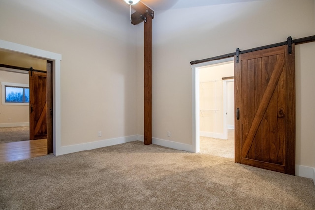 unfurnished room with baseboards, a barn door, and light colored carpet