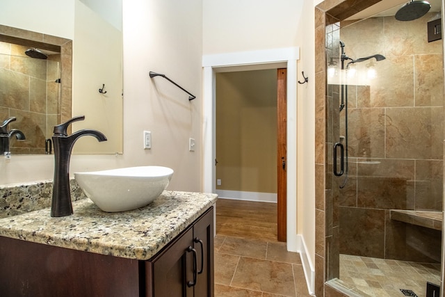 bathroom featuring stone finish floor, baseboards, a shower stall, and vanity