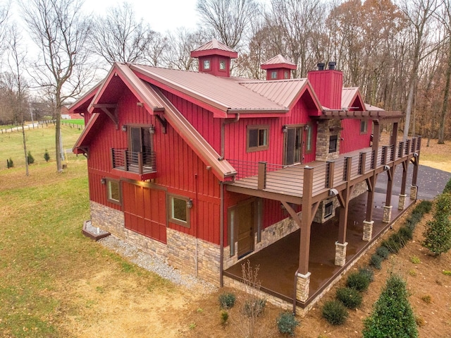 back of property with a lawn, stone siding, a chimney, metal roof, and board and batten siding