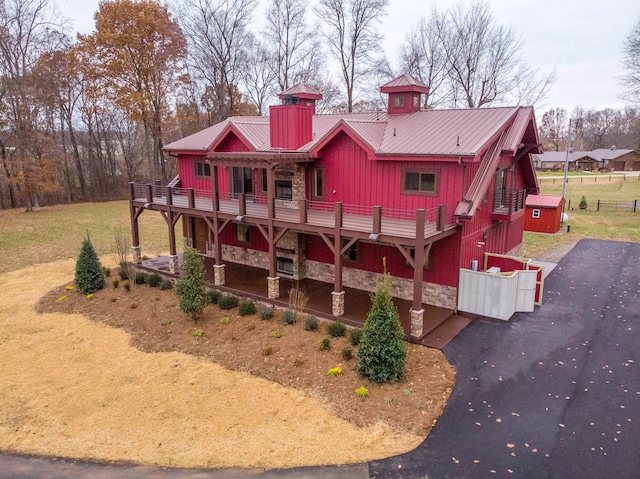 view of front of home featuring aphalt driveway, board and batten siding, metal roof, a deck, and stone siding