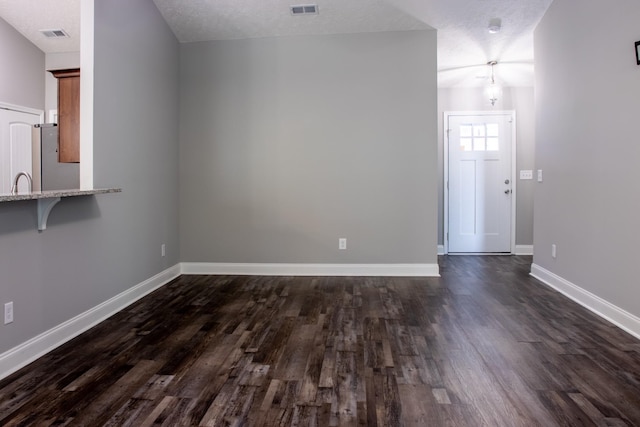 interior space with a textured ceiling, a sink, visible vents, baseboards, and dark wood-style floors