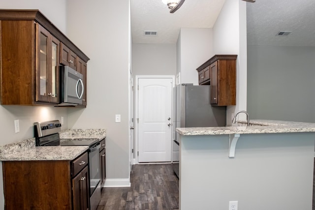 kitchen with a textured ceiling, stainless steel appliances, dark wood-type flooring, and glass insert cabinets