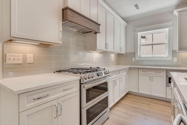 kitchen featuring range with two ovens, white cabinets, light wood-style floors, custom exhaust hood, and decorative backsplash