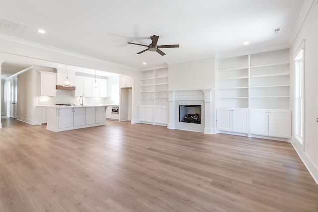 unfurnished living room featuring a fireplace, light wood finished floors, visible vents, ornamental molding, and ceiling fan