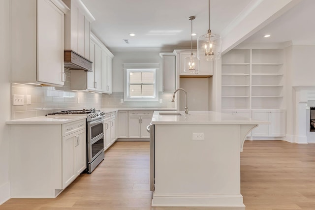 kitchen with a center island with sink, range with two ovens, light wood-style flooring, light countertops, and a sink