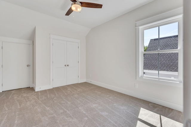 unfurnished bedroom with lofted ceiling, a closet, a ceiling fan, carpet flooring, and baseboards