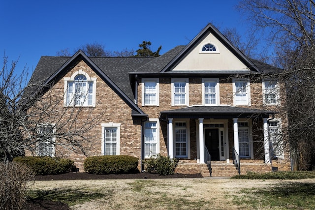 view of front of property with a shingled roof, brick siding, and a front lawn