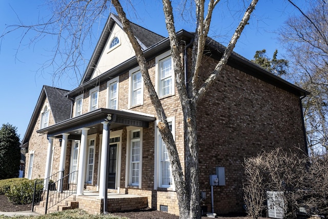 view of front of property featuring a shingled roof, covered porch, and brick siding