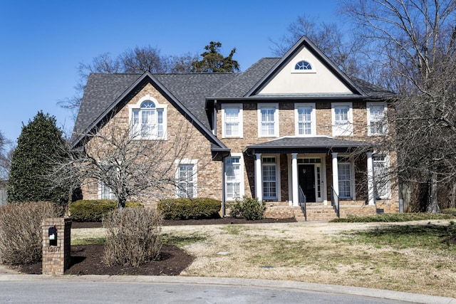 view of front facade featuring brick siding, a porch, and a shingled roof