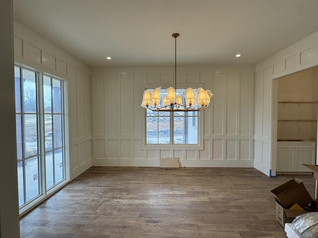 unfurnished dining area with recessed lighting, a notable chandelier, a decorative wall, and wood finished floors