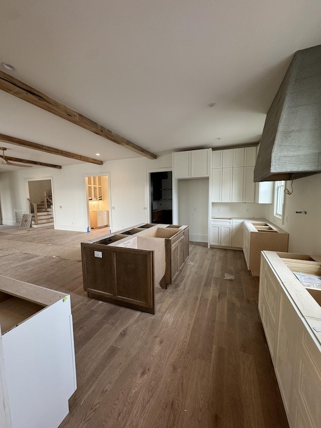 kitchen with open floor plan, beamed ceiling, wood finished floors, and white cabinetry