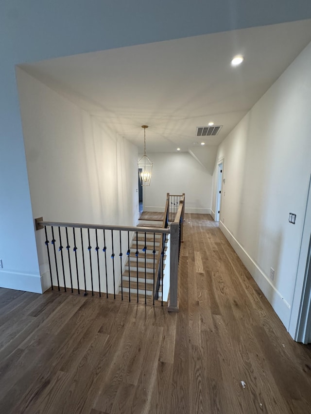 hallway with a chandelier, recessed lighting, wood finished floors, visible vents, and an upstairs landing