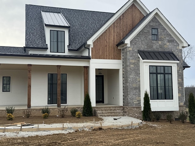 modern farmhouse style home featuring metal roof, a porch, a shingled roof, stone siding, and a standing seam roof