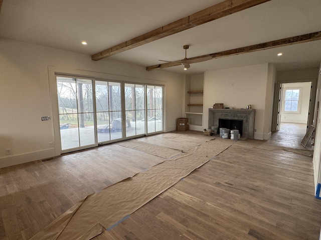 unfurnished living room featuring wood finished floors, beam ceiling, and baseboards