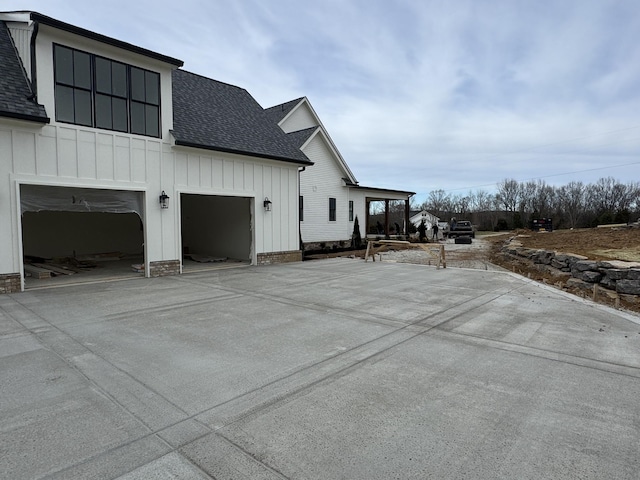 view of side of property with roof with shingles, board and batten siding, and driveway