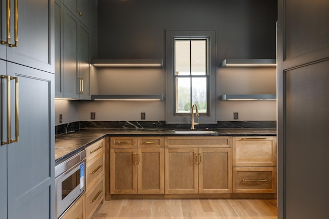 kitchen featuring light wood-style flooring, a sink, built in appliances, and open shelves