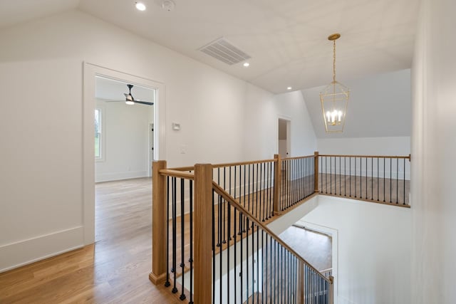 hallway with an upstairs landing, visible vents, wood finished floors, vaulted ceiling, and a notable chandelier