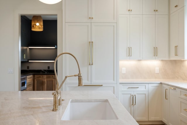 kitchen featuring light stone counters, a sink, and white cabinets