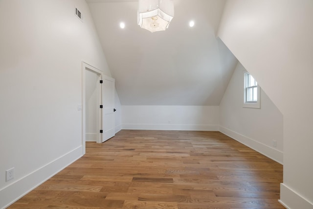 additional living space with baseboards, light wood-style flooring, visible vents, and vaulted ceiling