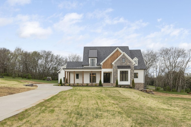 view of front of home featuring a standing seam roof, metal roof, stone siding, driveway, and a front yard
