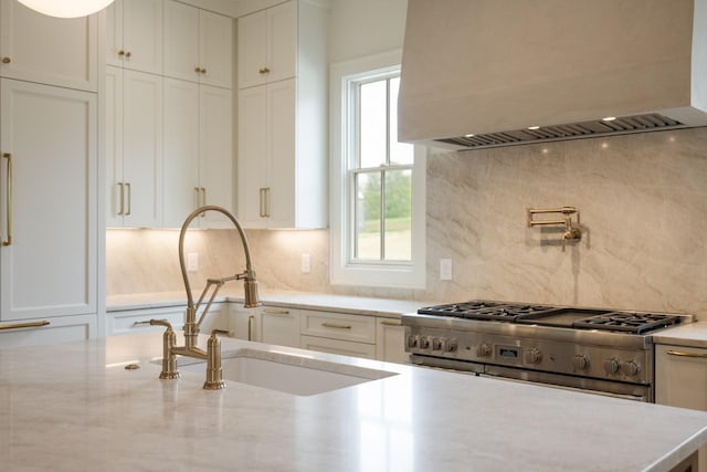 kitchen featuring custom range hood, high end range, white cabinetry, and a sink