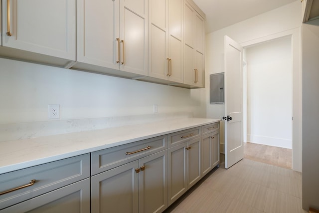 kitchen with electric panel, gray cabinetry, light stone countertops, and baseboards