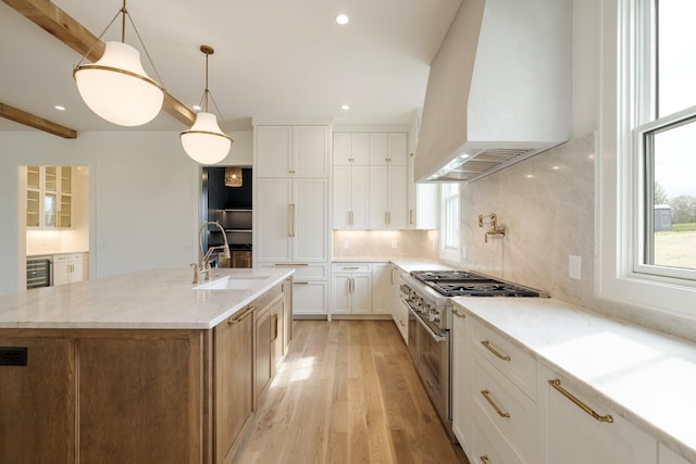 kitchen featuring premium range hood, wine cooler, stainless steel stove, a sink, and light wood finished floors