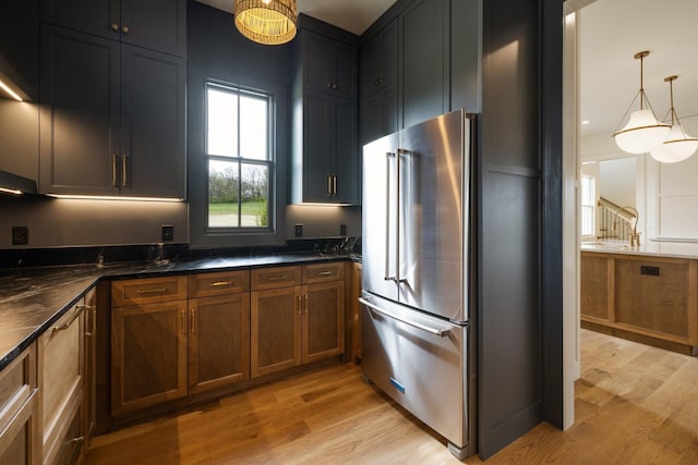 kitchen with a sink, light wood finished floors, high end fridge, hanging light fixtures, and brown cabinets