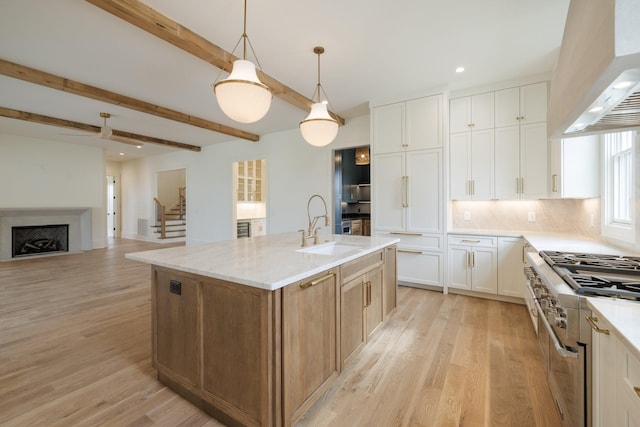 kitchen featuring custom range hood, a sink, light wood-style floors, beamed ceiling, and high end range