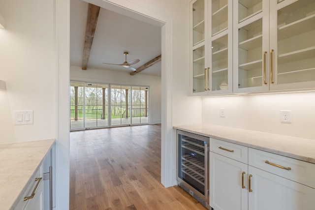 bar with wine cooler, beam ceiling, light wood-style flooring, ceiling fan, and a dry bar