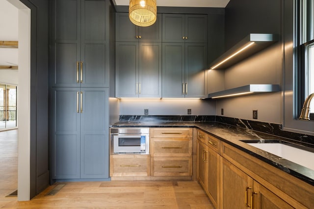 kitchen with light wood finished floors, a sink, dark stone counters, and oven