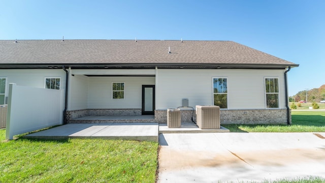 rear view of property featuring a lawn, roof with shingles, central air condition unit, a patio area, and brick siding