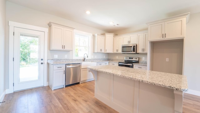 kitchen featuring stainless steel appliances, a kitchen island, a sink, light wood-style floors, and light stone countertops