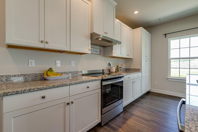 kitchen with dark wood-style floors, stainless steel electric stove, white cabinetry, under cabinet range hood, and baseboards