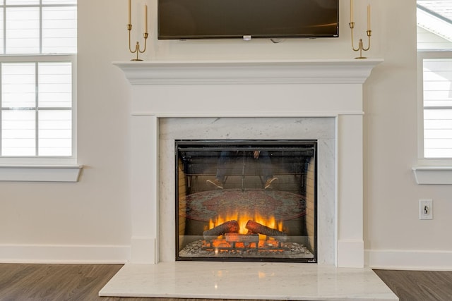 interior details with wood finished floors, a glass covered fireplace, and baseboards