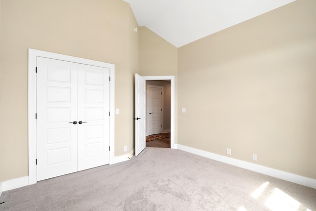 unfurnished bedroom featuring carpet floors, high vaulted ceiling, baseboards, and a closet