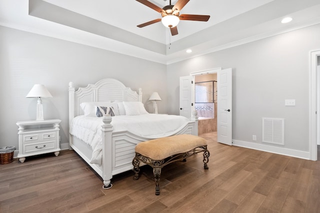 bedroom with a raised ceiling, visible vents, baseboards, and wood finished floors