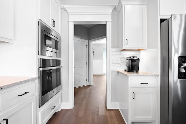 kitchen with light stone counters, dark wood-style floors, stainless steel appliances, decorative backsplash, and white cabinetry